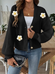 Detailed close-up of chunky black knit cardigan with 3D floral crochet appliques