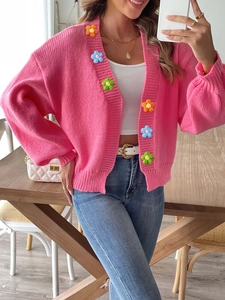 Detail of colorful hand-crocheted flowers on pink knit cardigan with thick knit texture