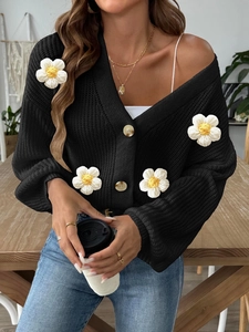 Detailed macro view of 3D crochet flower patches on a black knitted button-up cardigan