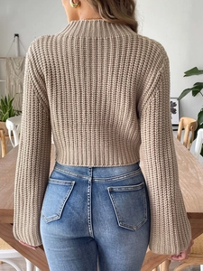 Back view of a cropped beige cable knit sweater featuring a stylish high collar design