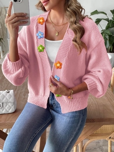 Detail of pink knitted cardigan featuring 3D floral appliques and ribbed texture knitwear