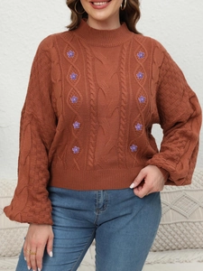 Detail of chunky cable knit texture and purple floral embroidery on brown lantern sleeve sweater