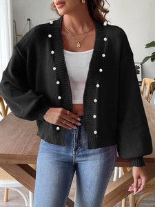 Detail of white pearl embellishments on a black knit cardigan with ribbed texture