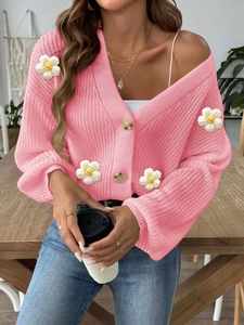Detailed view of pink knitted cardigan with 3D white crochet flowers and buttons