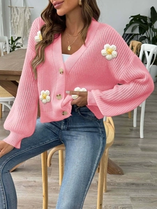 Close-up of pink knit cardigan with 3D white flower patches and amber buttons