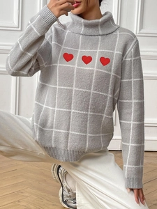 Detail of red heart embroidery and white grid texture on a grey turtleneck sweater