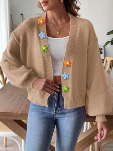Detail of beige knit cardigan featuring colorful 3D crochet flower appliques and texture