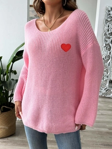 Detail of pink knit sweater featuring a vibrant red heart patch and U-neckline texture