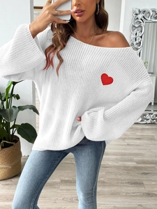 Detail of white off-shoulder knit sweater featuring red heart embroidery and cozy texture