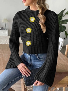 Women's black cropped knit sweater with crochet flowers and bell sleeves in a cozy setting