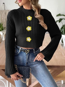 Detail of black cropped knit sweater featuring 3D floral embellishments and flared sleeves
