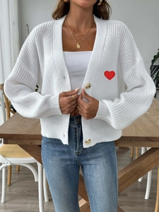 Dettaglio del ricamo a cuore rosso sul cardigan bianco in maglia con scollo a V