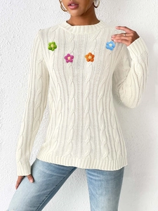Detailed close-up of handmade crochet flowers on a white cable knit sweater for women