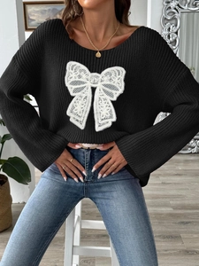 Dettaglio maglione nero in maglia con grande fiocco in pizzo bianco ricamato in rilievo