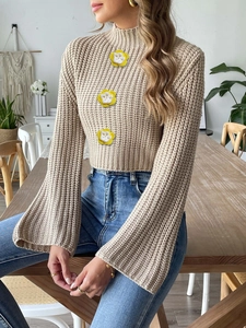 Detail of knit sweater showing beige texture and decorative floral crochet patches