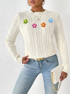Close-up of white cable-knit sweater featuring vibrant 3D crochet floral appliques