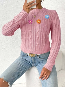 Close-up of pink knit sweater with colorful crochet flowers and textured cable pattern