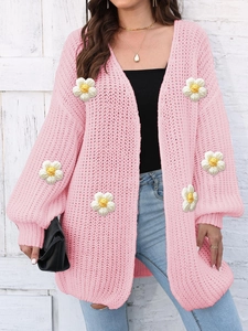Detail of pink knit cardigan with 3D floral accents and coarse texture on white wall