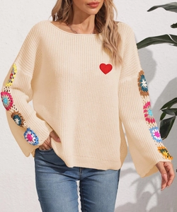 Detail of crochet flower patchwork and red heart patch on beige knit sweater sleeve