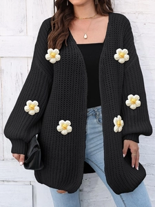 Detail of chunky knit black cardigan featuring white floral 3D appliqués and ribbed cuffs
