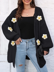 Close-up of chunky black knit cardigan featuring white 3D floral appliques and textures