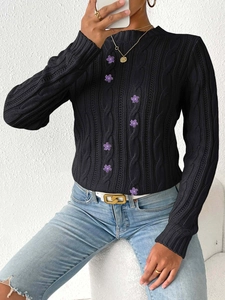 Detail of black cable-knit sweater featuring six decorative purple flower-shaped buttons
