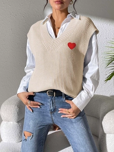 Detalle de un chaleco de punto beige con cuello en V y un parche de corazón rojo bordado