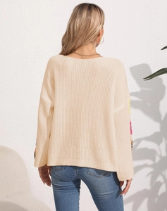 Detailed view of cream knit sweater featuring colorful floral embroidery on the back sleeves