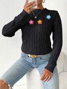 Close-up of black cable knit sweater with handmade pink and orange crochet flower patches