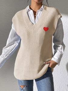 Detalle del tejido del chaleco beige con cuello en V y bordado de corazón sobre camisa