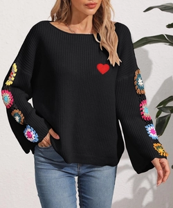 Detail of colorful crochet floral embroidery and red heart patch on black knit sweater