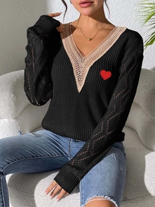 Détail d'un pull en tricot noir à col en V avec bordure dentelle beige et broderie cœur