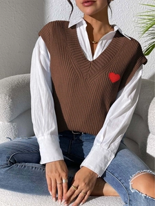 Detail of red heart embroidery on brown V-neck knit vest paired with white shirt