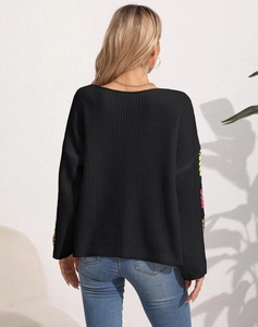 Detailed back view of loose knit sweater with vibrant floral embroidery on sleeves
