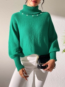 Detail of green turtleneck knit sweater featuring delicate white pearl embellishments