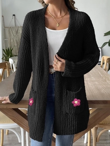 Détail d'un cardigan noir en maille avec une fleur au crochet rose sur la grande poche