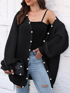 Detail of chunky black knit cardigan with elegant white pearl accents and thick texture