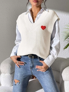 Detalle del bordado de corazón rojo en un chaleco de punto blanco con cuello en V
