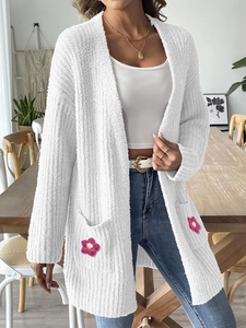 Détail d'une fleur rose crochetée main sur la poche d'un gilet blanc