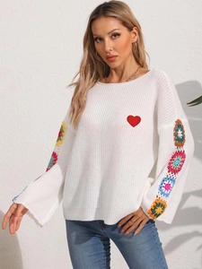 Detail of colorful crochet floral patterns on sleeves and red heart patch on white sweater