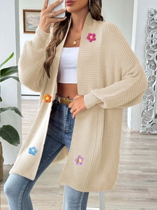 Détail d'un cardigan en maille beige avec fleurs 3D au crochet et une coupe ouverte ample