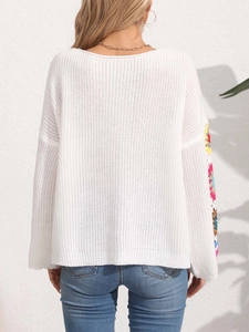 Detail of colorful crochet knit patterns on sleeves of a white off-shoulder sweater