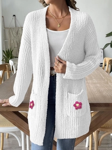 Détail du cardigan blanc montrant la maille bouclée et la fleur rose au crochet sur la poche