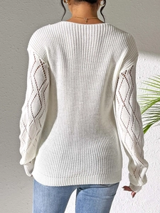 Détail d'un pull blanc à manches longues montrant des motifs tricotés ajourés aux manches