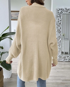 Detail view of the back of a beige oversized knitted sweater with high collar and ribbed cuffs