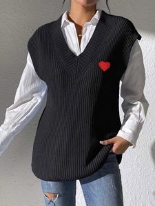 Detalle del chaleco de punto negro con cuello en V y parche de corazón rojo bordado en el pecho