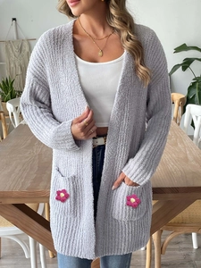 Détail du cardigan en maille lilas avec des poches décorées de fleurs crochetées roses