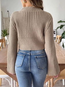 Détail d'un pull court en maille côtelée beige avec manches évasées et jean taille haute