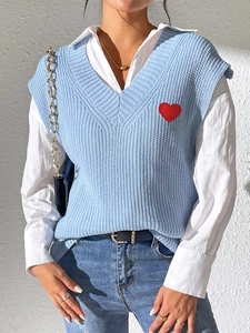 Detalle de chaleco de punto azul claro con cuello en V y parche de corazón rojo bordado