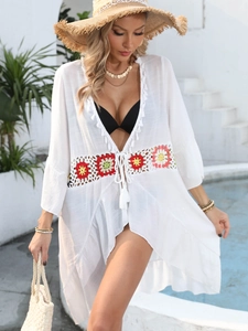 Détail d'un cache-maillot blanc avec broderie florale colorée et bordures à pompons